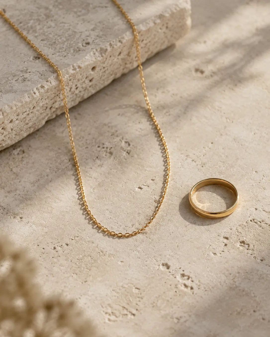 Plain gold chain and ring on pale stone.